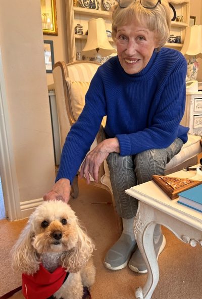 An older lady sits on a chair petting a small white dog
