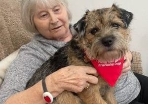 An older lady sat on a chair holding a border terrier